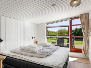 Ein Schlafzimmer mit einem Bett, einem Nachttisch, einer Wandleuchte und einer Glastür, die auf eine Terrasse im Freien führt.