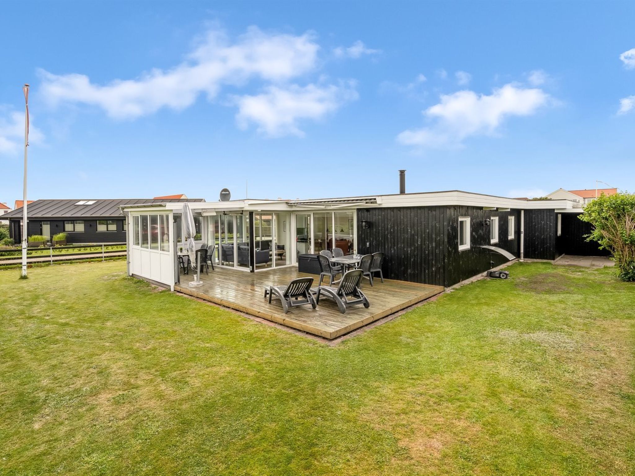 A modern house with a covered patio, a lawn, and a neighboring building.