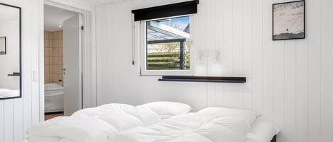 A bedroom with a bed, a window with a view, a mounted shelf, and a framed picture on the wall.