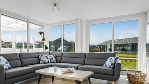 A modern living room with a sectional sofa, a wooden coffee table, and large windows offering a view of the outside. - "Myrte" - 300m from the sea by Interhome (Blokhus)