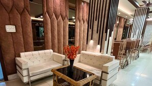 A modern lobby with a white sofa set, a wicker coffee table, and vertical wooden panels. - Hotel Meghnath Palace (Jalpaiguri)