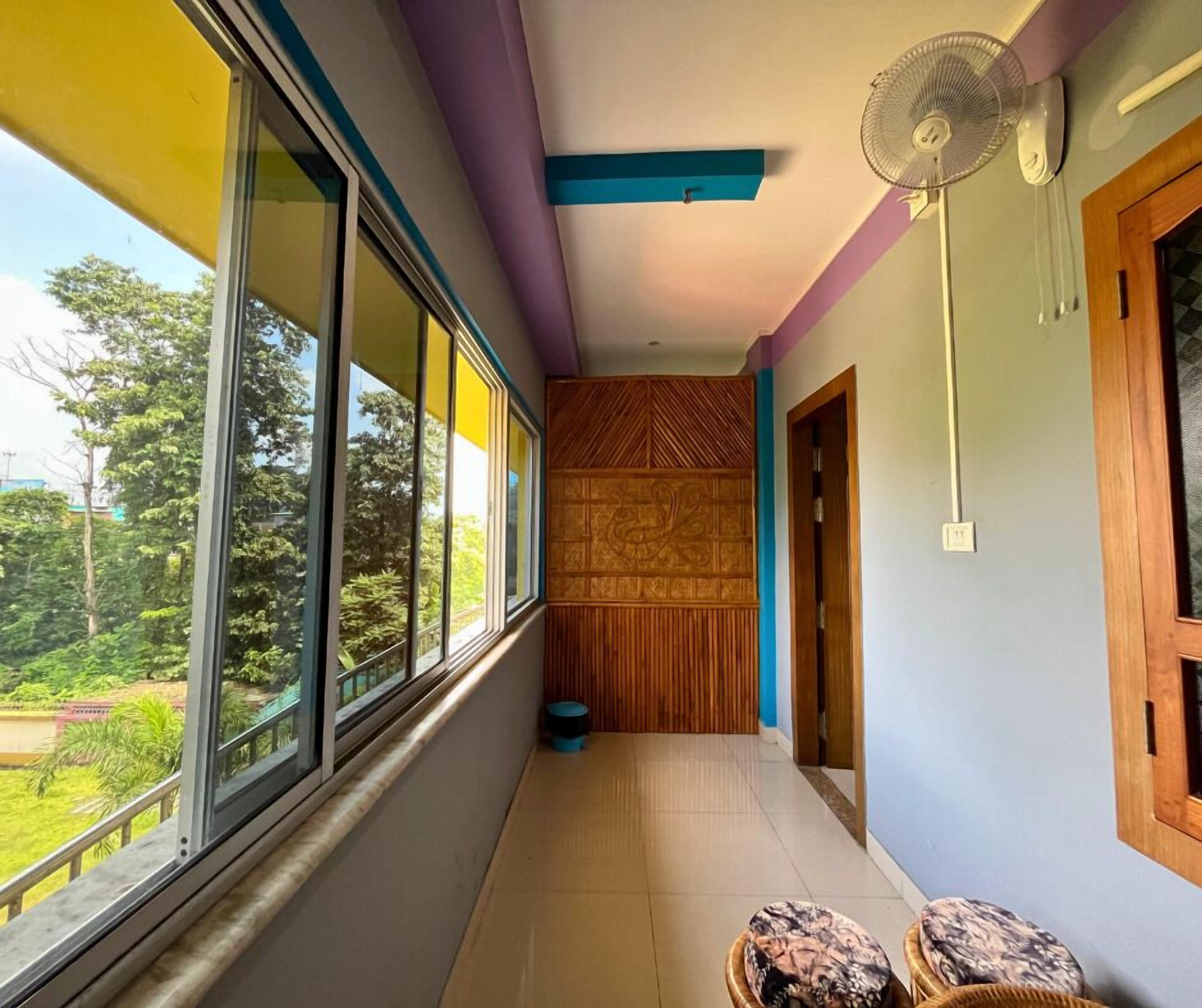 Ein schmaler Korridor mit Blick auf Grünflächen, eine Holzwand mit geometrischen Mustern und ein Deckenventilator.