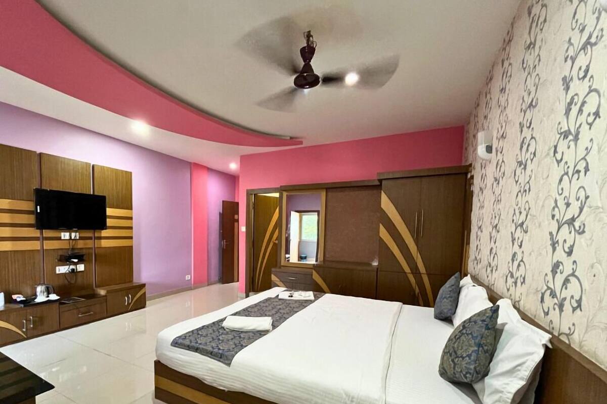 Quarto moderno com uma cama grande, uma TV fixada na parede e um guarda-roupa com espelho.