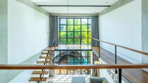 Un intérieur moderne avec un escalier menant à un balcon, de grandes fenêtres et un luminaire suspendu.