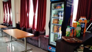 Una zona de estar con una mesa y sofás, un refrigerador Pepsi lleno de bebidas, y una encimera con diversos artículos.