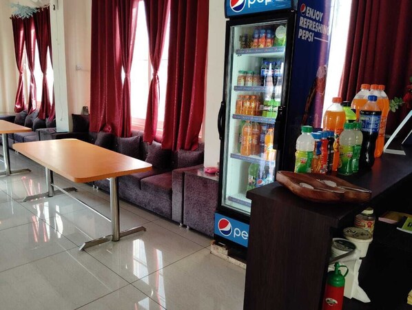 Un espace détente avec une table et des canapés, un réfrigérateur Pepsi rempli de boissons et un comptoir où sont exposés divers articles.