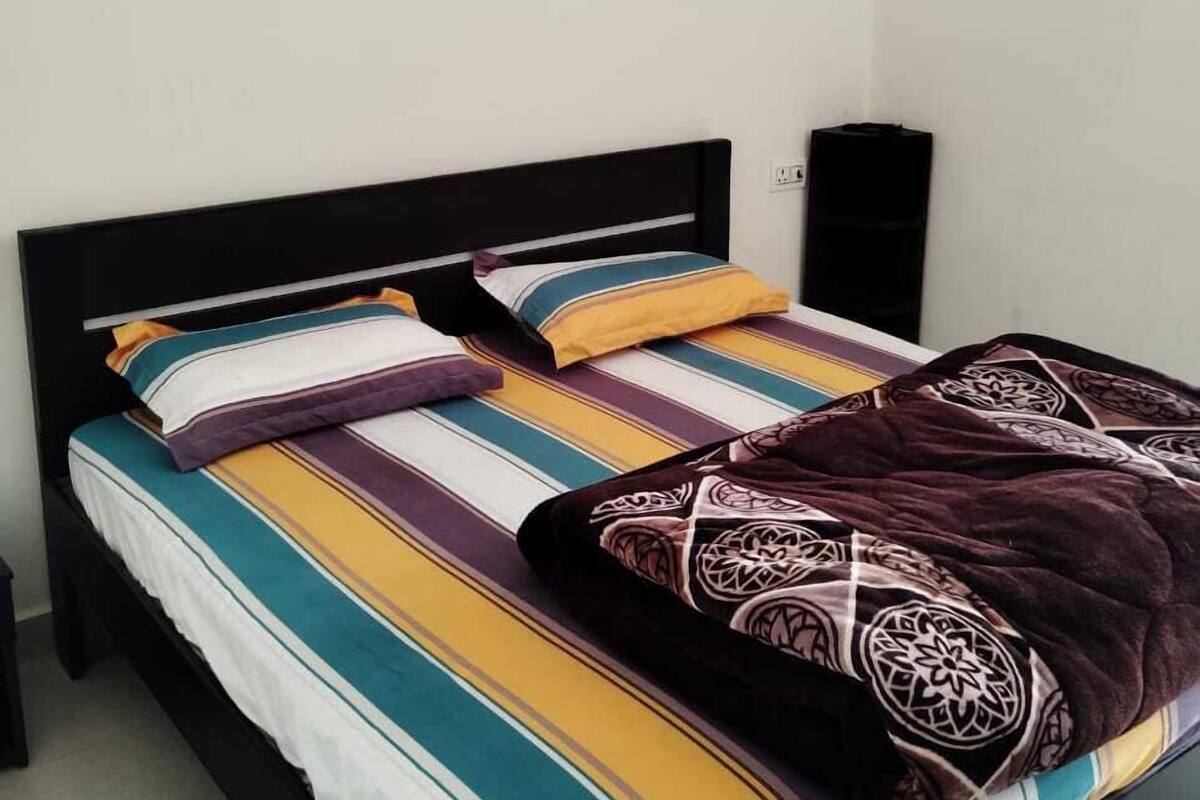 Una cama con estructura negra, ropa de cama a rayas y una manta decorada.