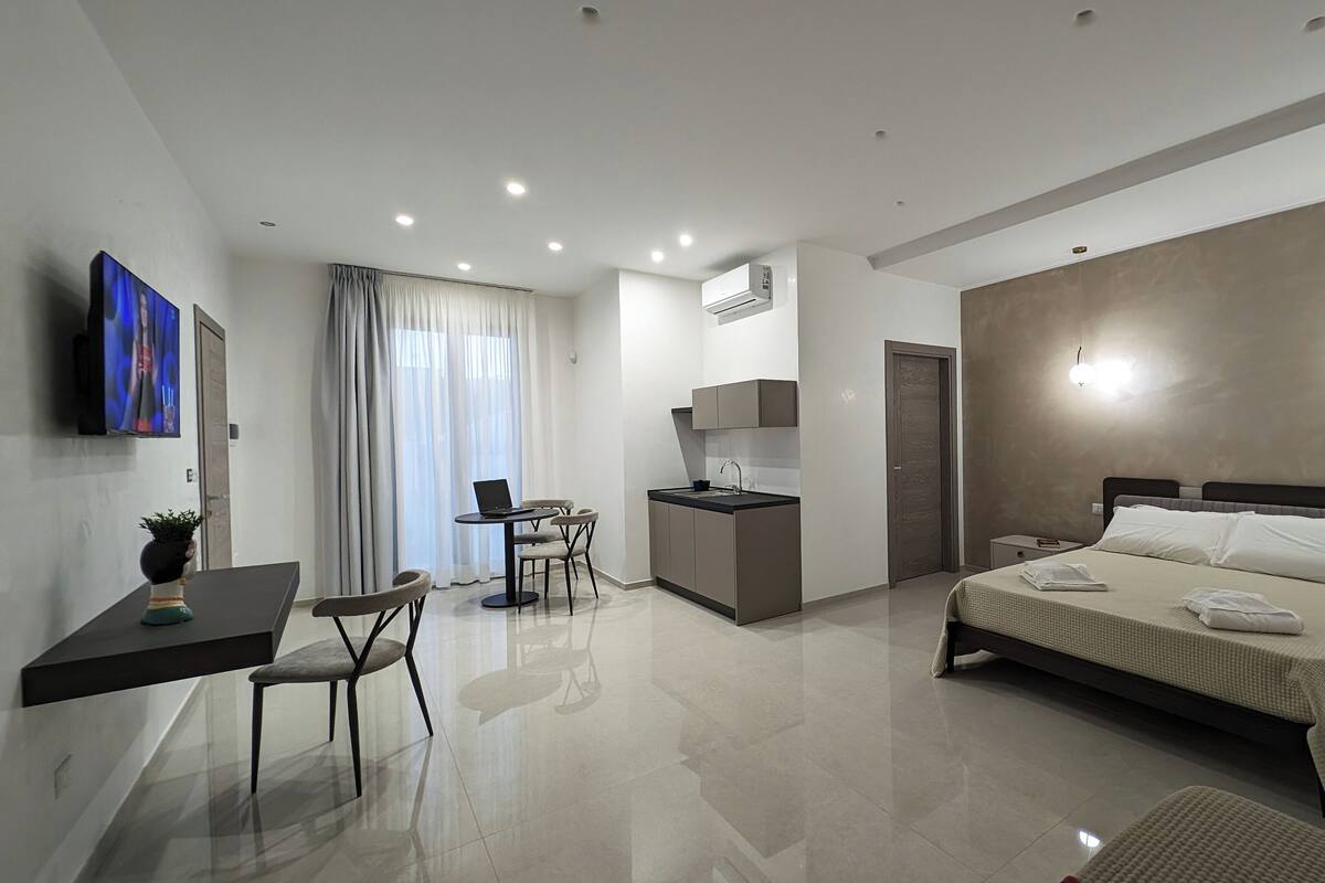 A modern hotel room with a bed, bedside table, and a desk with a laptop.