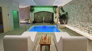 Un área de piscina con una estatua, sillas de descanso blancas y una mesa con una botella.