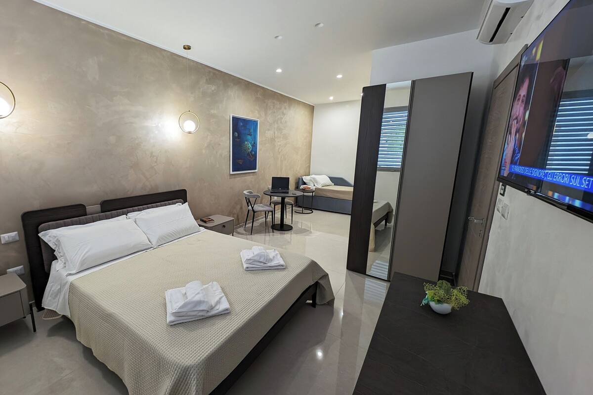 A modern hotel room with a large bed, bedside tables, a desk, and a TV.