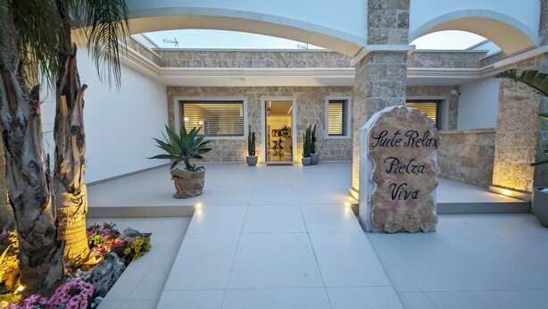 Entrada de hotel con un arco de piedra, plantas en macetas y un letrero que dice "Suite Relax Pietra Viva".