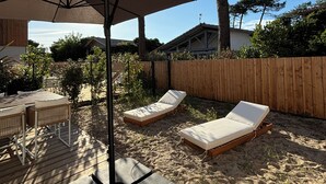 A backyard with a wooden deck, two lounge chairs, a table with chairs, and a large umbrella.