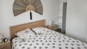 A bedroom with a bed, a bedside table with a lamp, a wall-mounted fan, and a wardrobe.