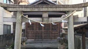 Un portail torii japonais traditionnel, orné d’une corde et de décorations en papier blanc, qui mène à un portail en bois.