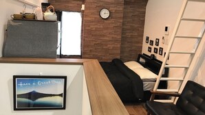 Une chambre d’hôtel de taille réduite, comprenant un lit, un bureau, une chaise, une échelle et une horloge murale.