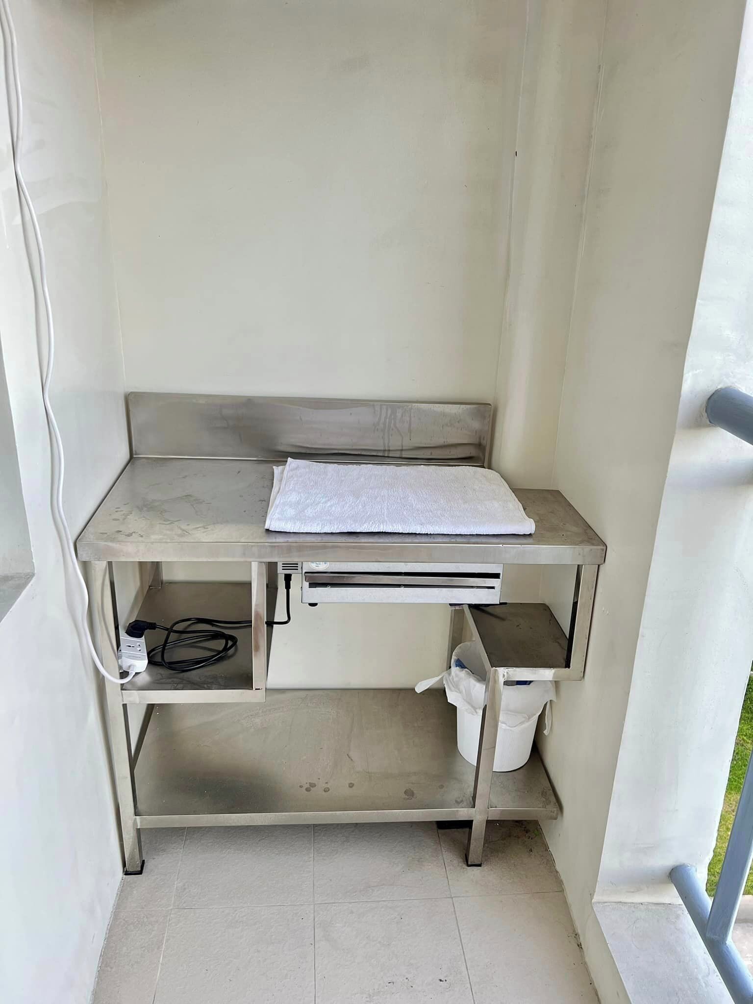 A small, clean room with a metal desk, a white towel, and a trash bin.