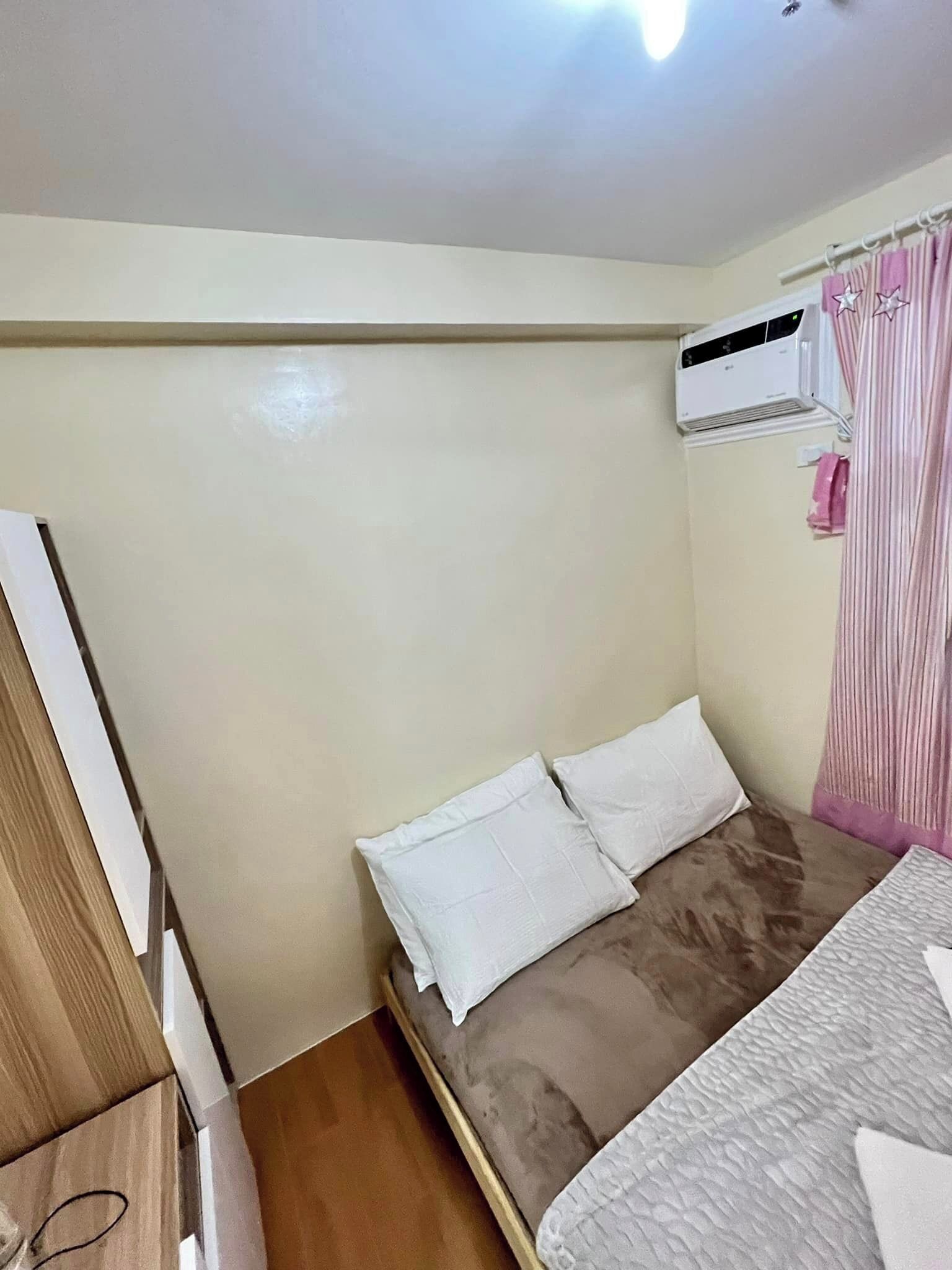 Une petite chambre avec un lit simple, une armoire en bois, un oreiller blanc, un matelas marron et une couette blanche.