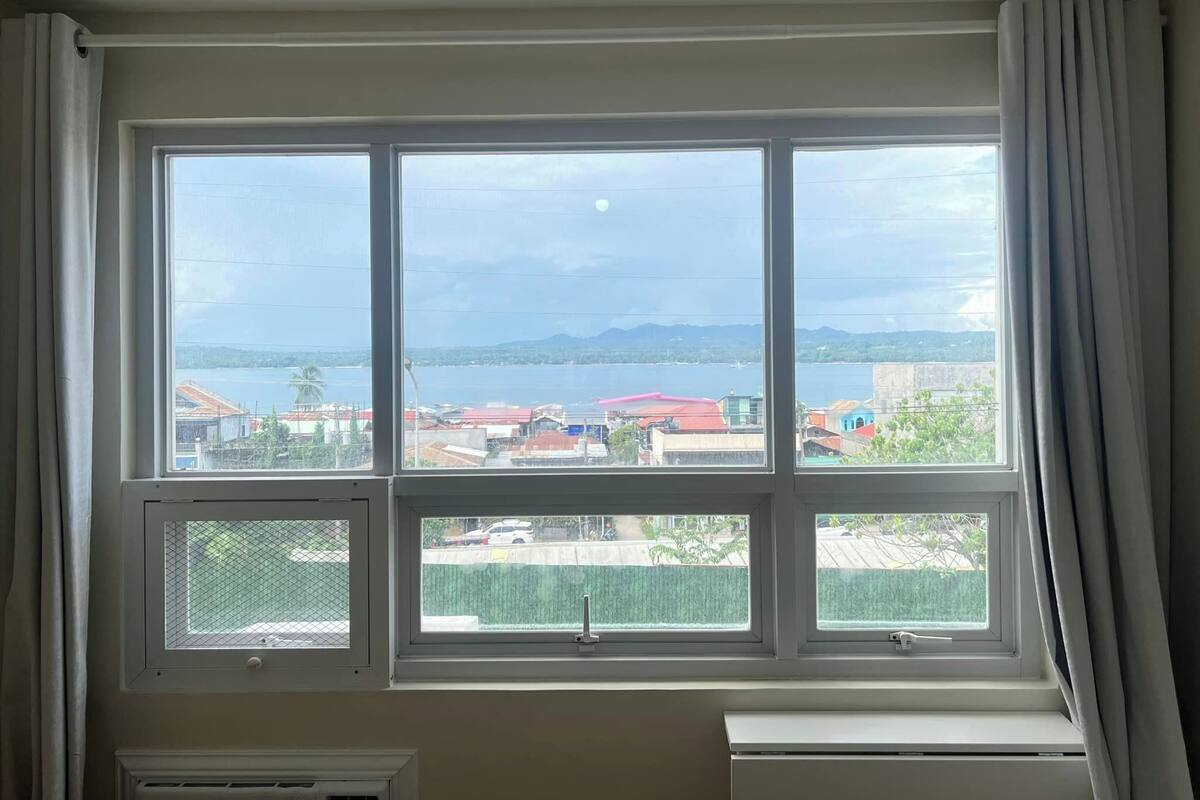 A room with a large window overlooking a body of water and distant mountains.