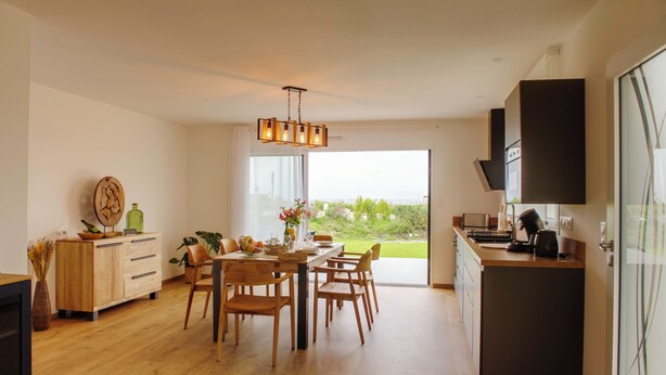Una cocina moderna con armarios de madera, un comedor con mesa y sillas de madera, y un ventanal con vistas a zonas verdes.