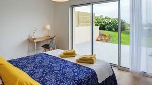 Un dormitorio con cama, escritorio y vista a un jardín a través de un ventanal corredero.