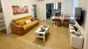 A living room with a sofa, coffee table, and dining table with chairs. There is a kitchen in the background. - A few steps from the historic center and Vatican (Roma)