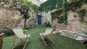 A courtyard with artificial grass, two wooden chairs, a stone wall, and a door. - ANGE & LICE" HOUSE PERNES-LES-FONTAINES (Pernes-les-Fontaines)