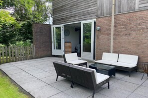 Relax on the patio with wicker sofas and a coffee table, surrounded by a lush lawn and trees.