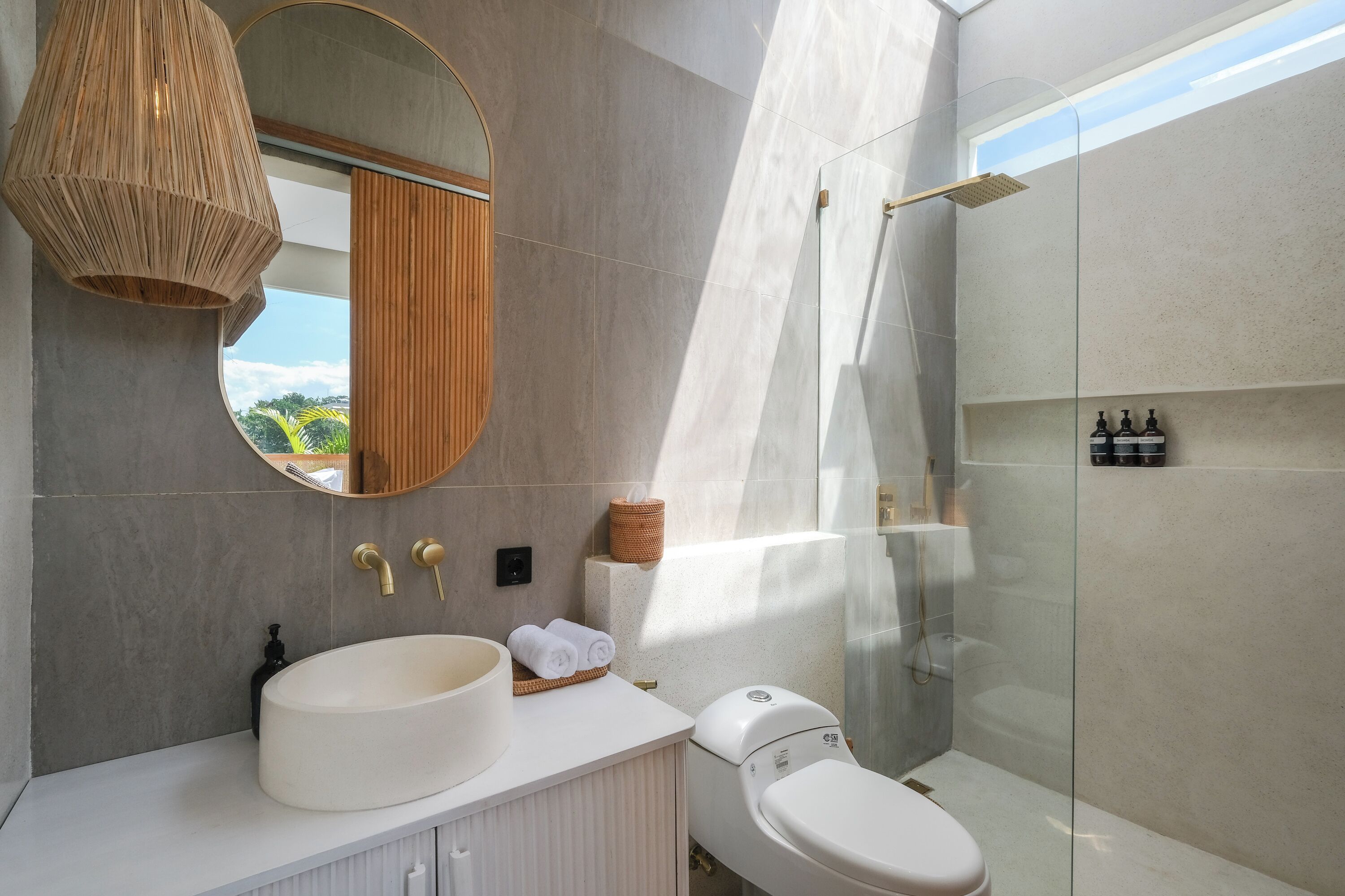 A modern bathroom with a round mirror, a large sink, a toilet, and a glass-enclosed shower.