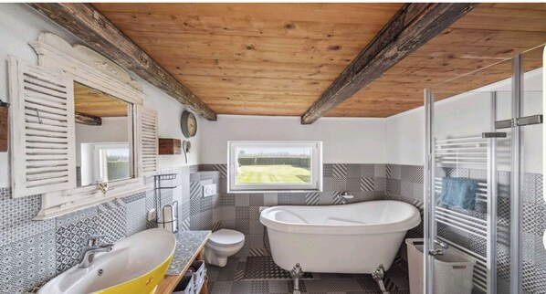 A bathroom with a bathtub, toilet, sink, and a window with a view of a field.
