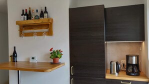 A kitchen with a wooden table, wine bottles, a coffee maker, and a potted plant.