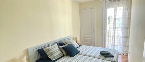 A bedroom with two beds, a nightstand, a ceiling fan, and a door leading to a balcony.