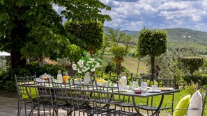 An outdoor dining area with a table set for four, surrounded by greenery and hills in the background. - Villa Loredana 12 Emma Villas (Montaione)