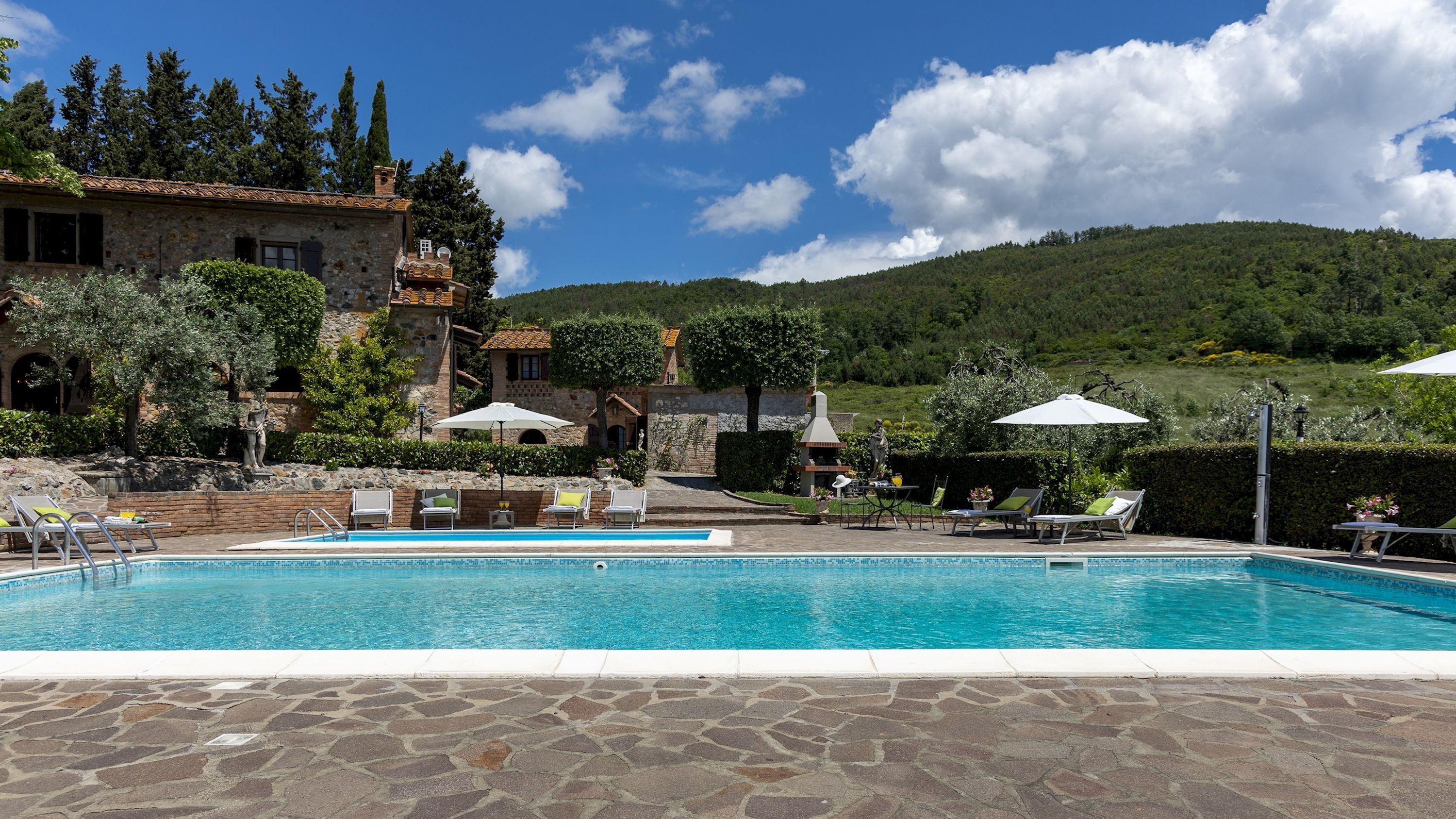 A pool area with lounge chairs and umbrellas, surrounded by stone walls and greenery.
