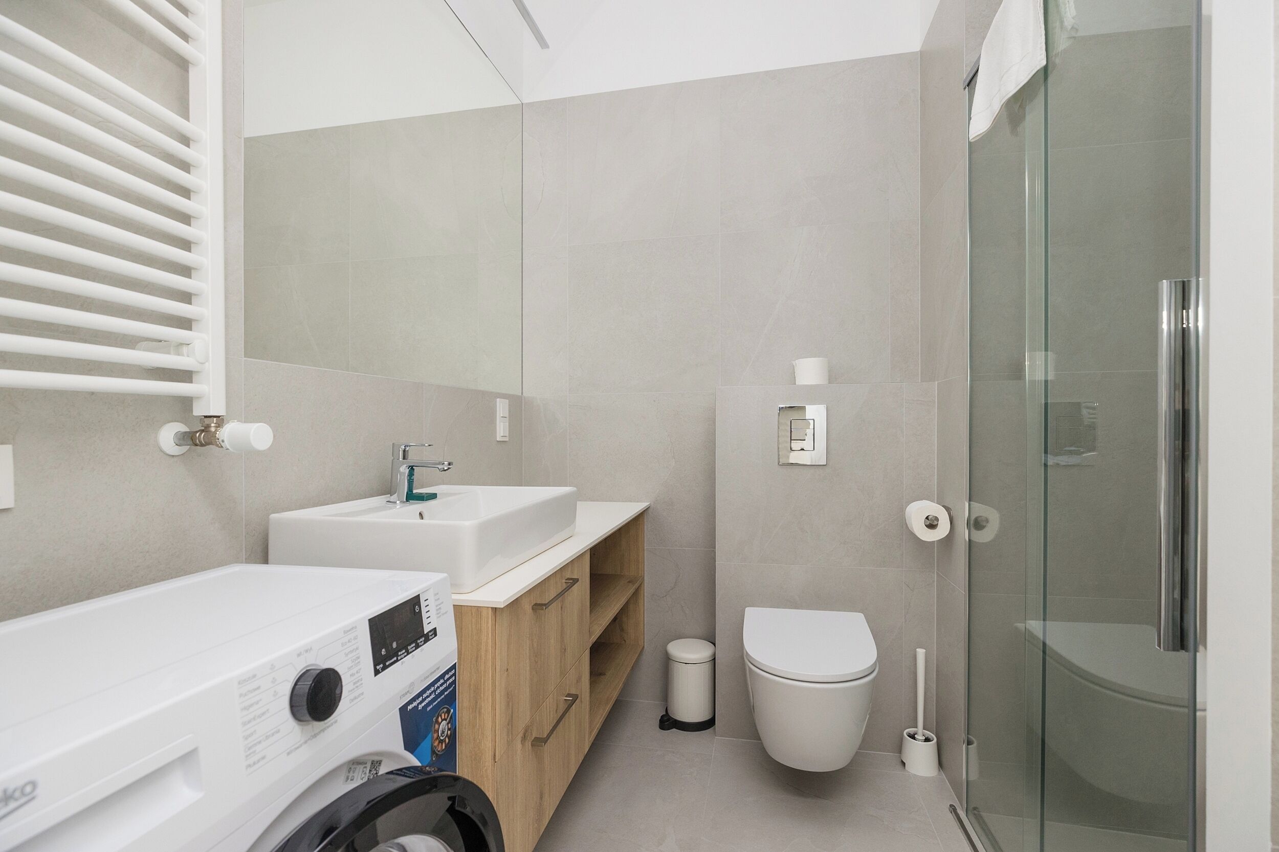 A modern bathroom with a glass shower enclosure, a built-in sink, and a washing machine.