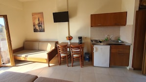 Een ruimtelijke leefruimte met een kitchenette, een eethoek en een bank.