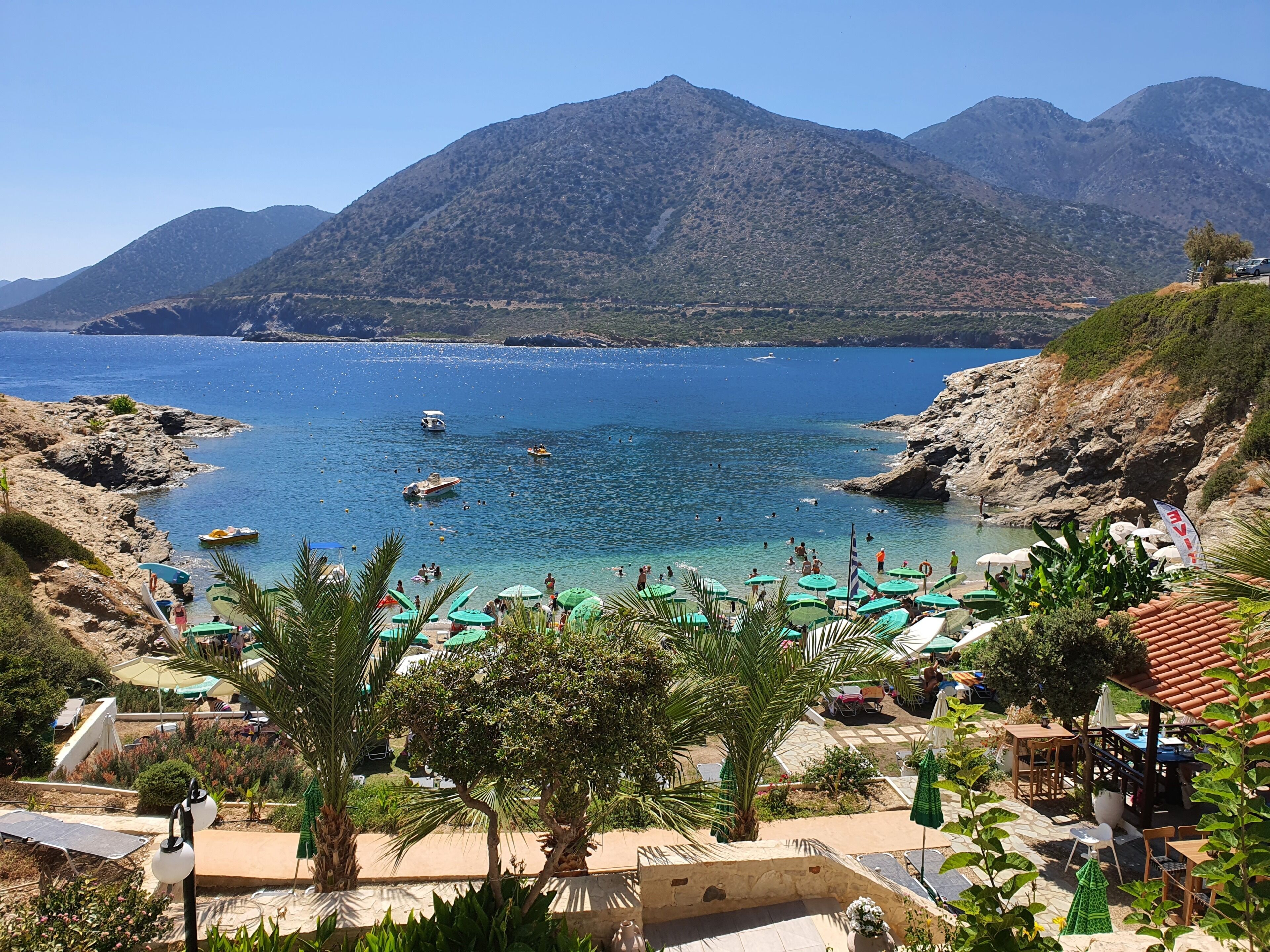 A coastal resort with a beach, umbrellas, and a mountainous backdrop.