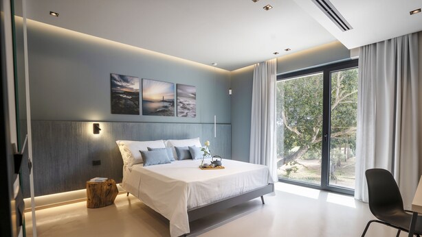 Un dormitorio moderno con una cama grande, una mesita de noche de madera y vistas al exterior a través de un ventanal corredero.