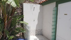 Un petit espace de douche fermé, doté d’un sol carrelé, d’une porte verte et d’un seau blanc posé sur le sol.