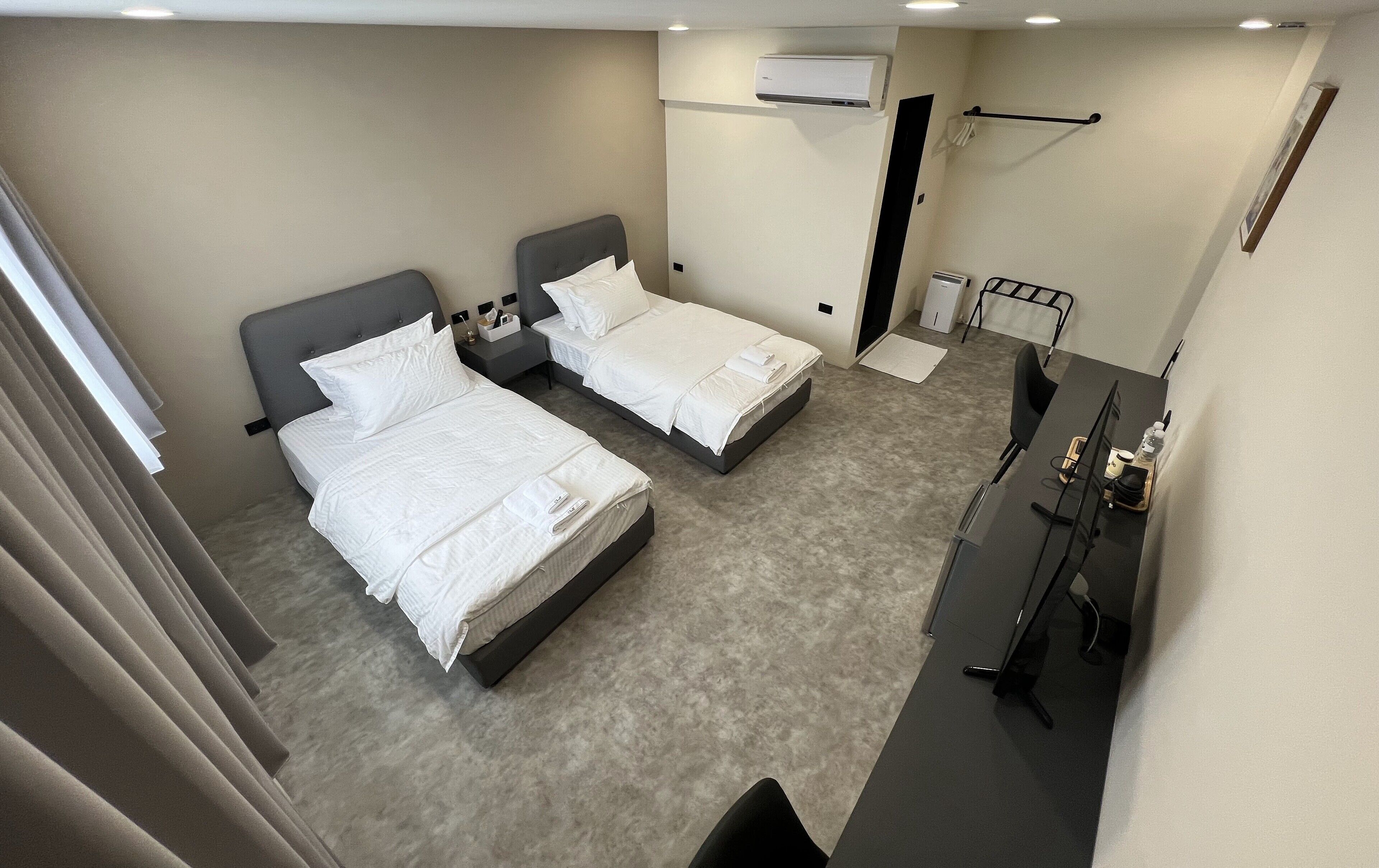 Habitación de hotel con dos camas, un escritorio, una silla, unidad de aire acondicionado y un baño pequeño.
