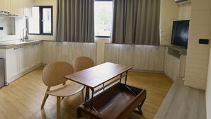 Een kleine keuken met een eethoek, een aan de wand bevestigde televisie en een raam met gordijnen.