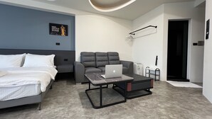 Een moderne hotelkamer met een bed, een grijze bank, een klein tafeltje met een laptop en een poster aan de muur.