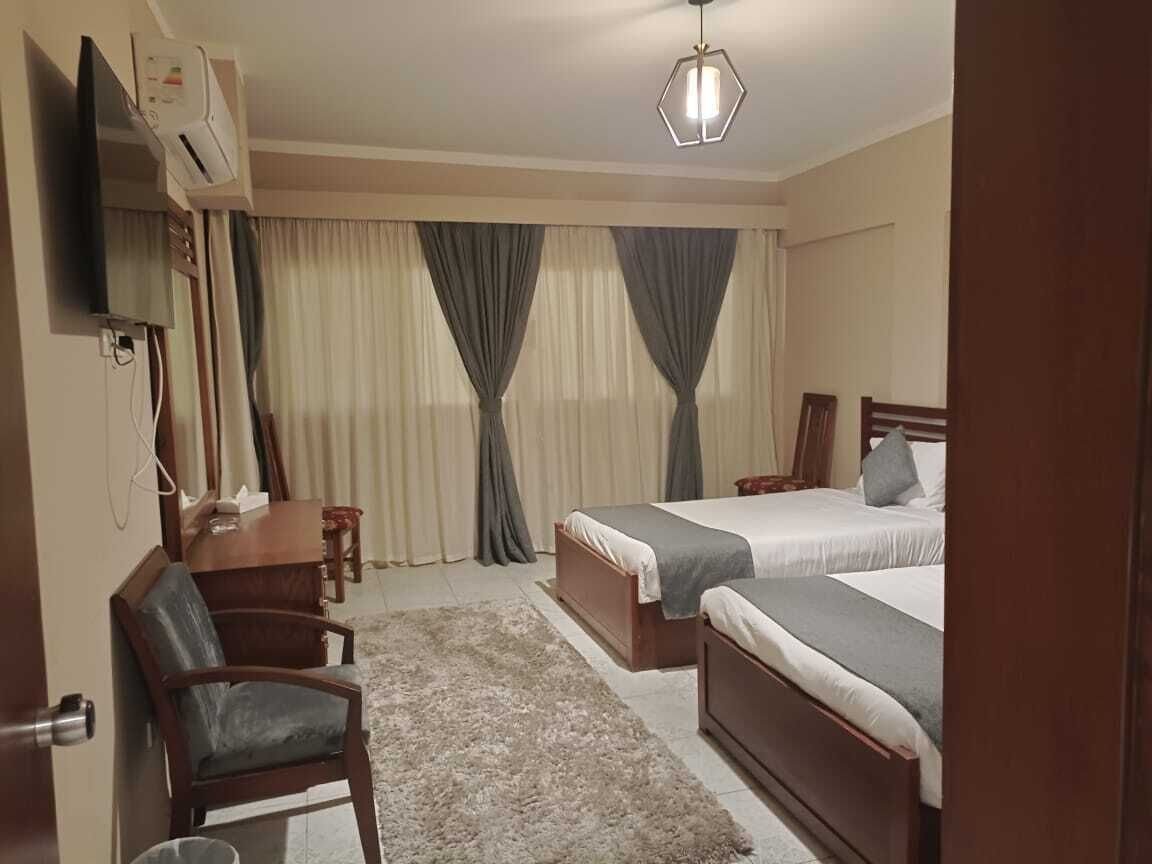 A hotel room with two beds, a desk, a chair, an air conditioning unit, and a television.