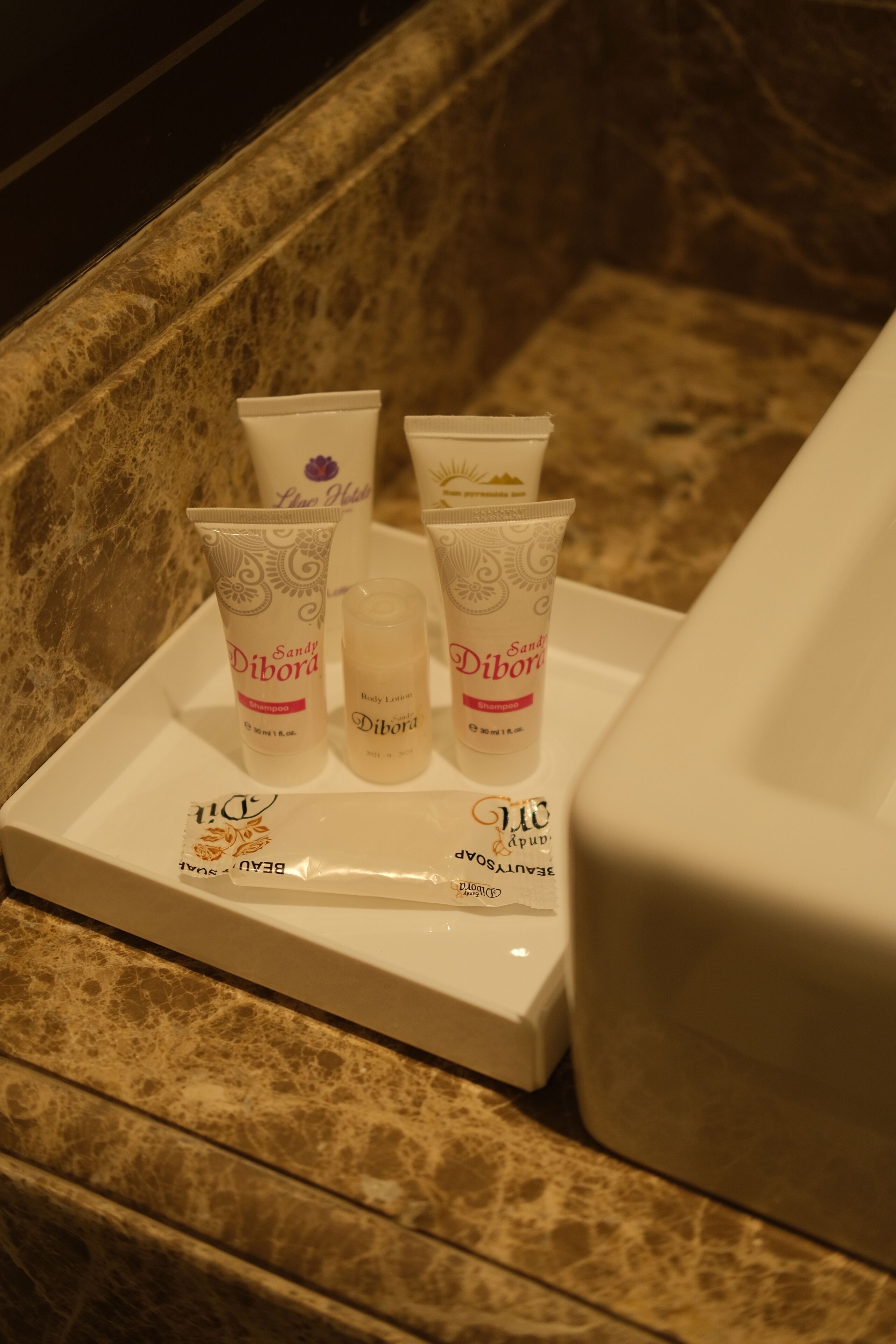A tray with four bottles of 'Sand Dibora' body lotion and shampoo, and a 'Beau Soleil' facial serum.