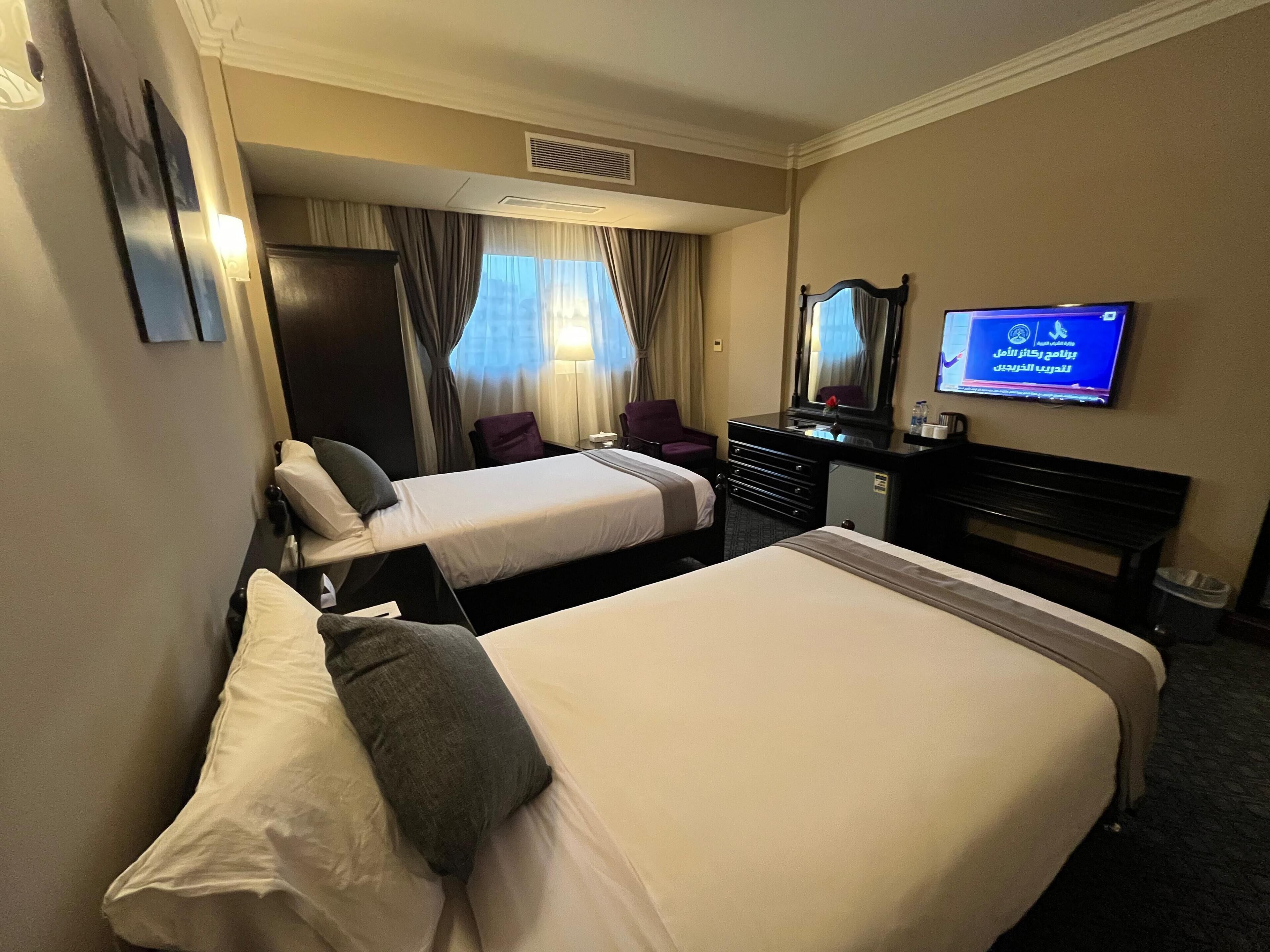 A hotel room with two beds, a desk, a chair, a television, and a mirror.