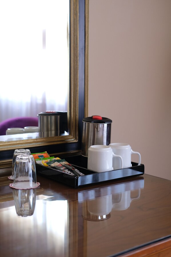 Une chambre d’hôtel avec un bureau en bois, une machine à café, deux tasses blanches, un verre et un plateau avec des sachets de thé.