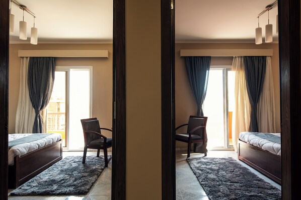 A hotel room with a bed, a chair, a desk, and a view of the outside. - Marwa Palace Hotel (Giza)