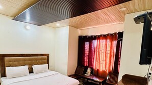 Un dormitorio con una cama de madera, una mesita pequeña, una silla, un tapete morado y un televisor sobre un mueble de madera.