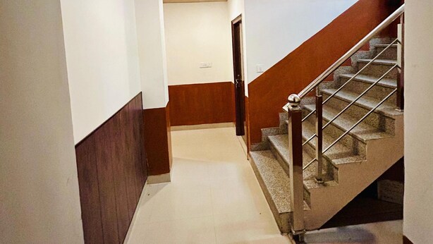 Un pasillo con techo de madera, una escalera con barandillas de metal y piso de baldosas.