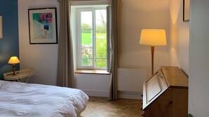 Una camera da letto con un letto, una finestra con tende, una lampada, un termosifone e un quadro appeso al muro.