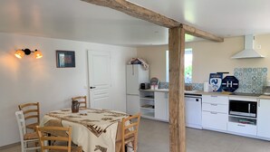 Zona pranzo con tavolo apparecchiato per quattro, cucina con mobili bianchi, macchina da caffè e cartello che indica un albergo.
